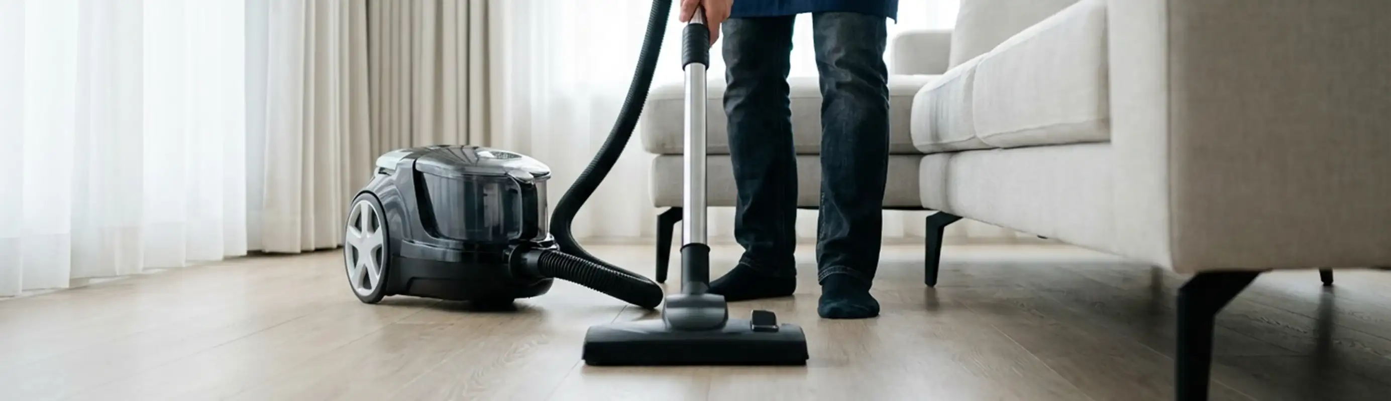 Professional house cleaner vacuuming a living room floor with a canister vacuum cleaner, Santa Ana, CA.