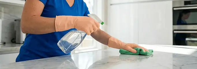 Maid service worker spraying and wiping a kitchen countertop with a microfiber cloth for sanitizing, Santa Ana, CA.