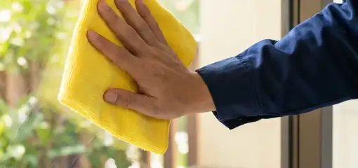 House cleaner wiping a glass window with a yellow microfiber cloth for streak-free cleaning, Santa Ana, CA.